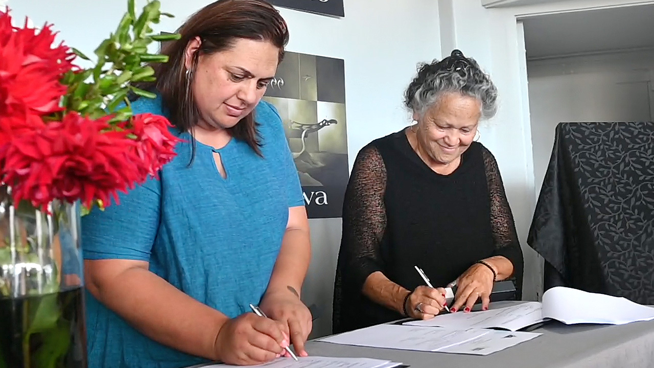Katie Murray and another woman signing the strategic partnership agreement between Oranga Tamariki and Te Kahu Oranga Whānau in Kaitaia